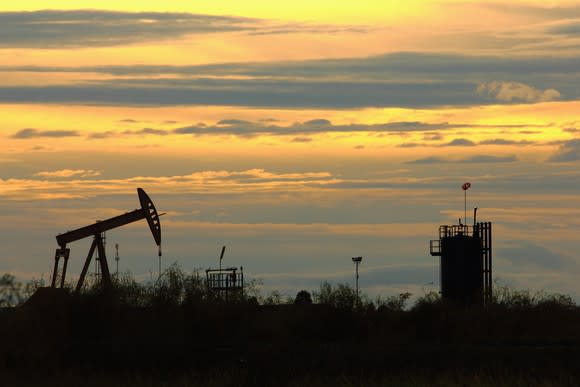 An oil pump in a grassy field at sunset.