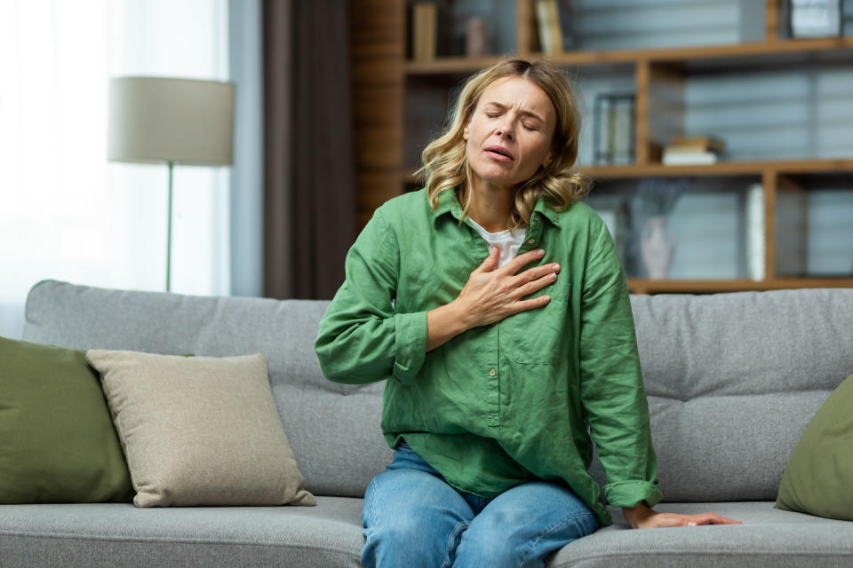 Heart attack, panic attack,. An elderly woman sits on the sofa at home and holds her hand to her chest. It is difficult to breathe, feels severe pain.