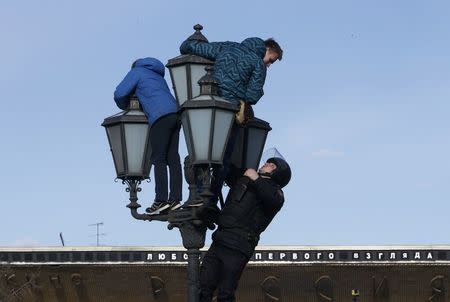 A riot police officer climbs on a lamp pole to detain opposition supporters during a rally in Moscow, Russia March 26, 2017. REUTERS/Sergei Karpukhin