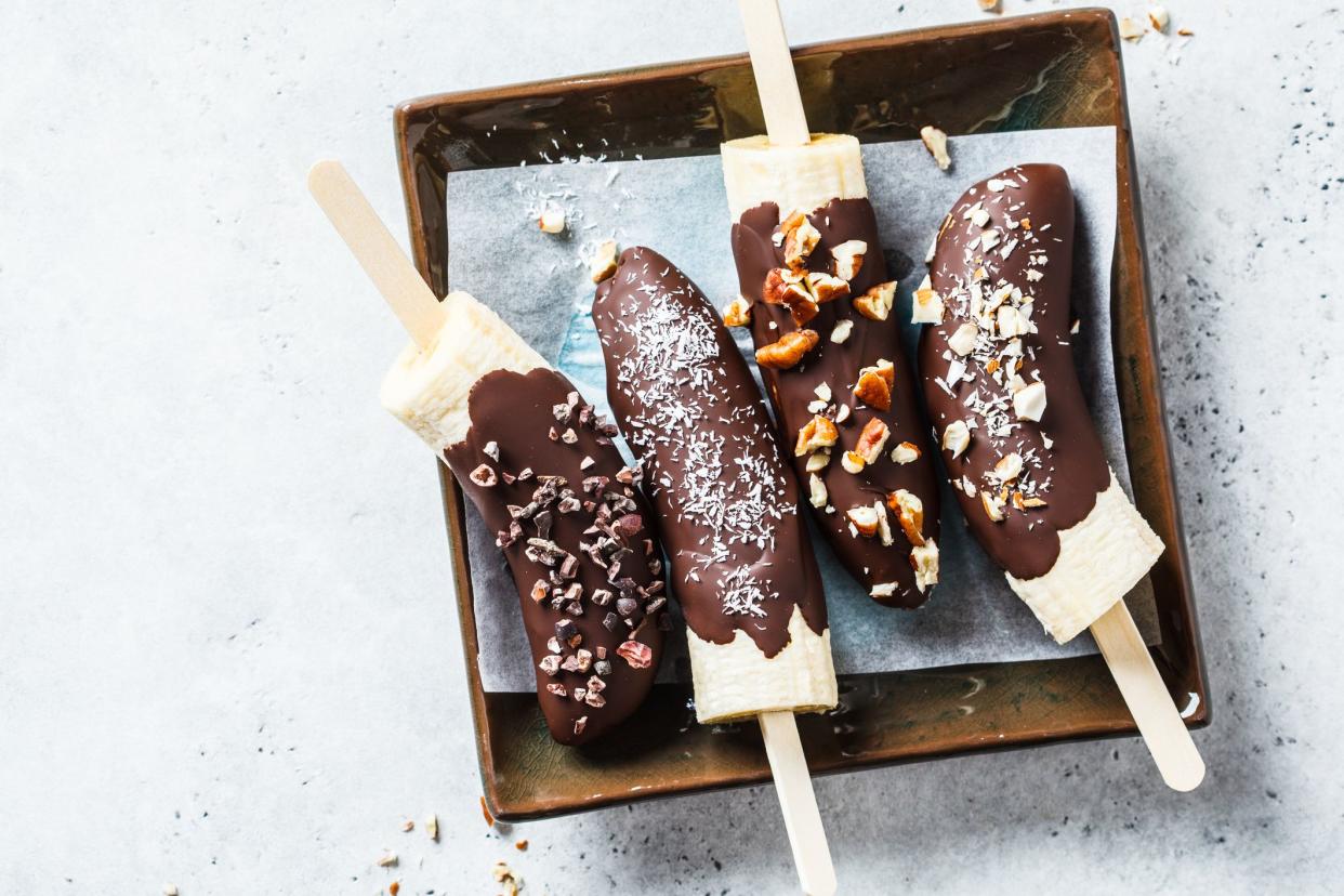 Four frozen chocolate bananas on a brown square plate on a light grey background