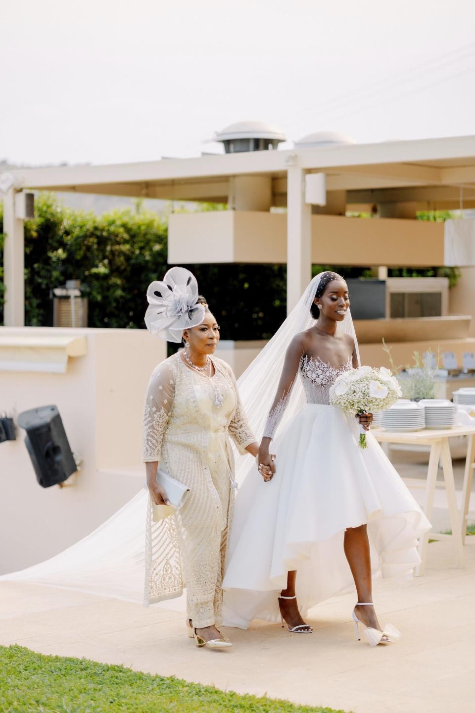 A bride and her mother hold hands as they walk down the aisle.