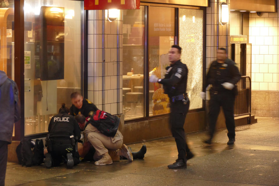 FILE - In this Jan. 22, 2020, file photo, officers attend to one of several shooting victims outside of McDonald's on Third Avenue in Seattle. The window of the restaurant behind them was shattered after a gunman opened fire in the heavily trafficked downtown area. Two men who investigators say were involved in a downtown Seattle shooting that killed one person and injured several others were arrested Saturday, Feb. 1, the Seattle Police Department said. The Seattle Times and the Las Vegas Review-Journal report that Marquise Tolbert, 24, and William Tolliver, 24, were booked into jail in Clark County, Nevada, according to jail records. (David Silver via AP, File)