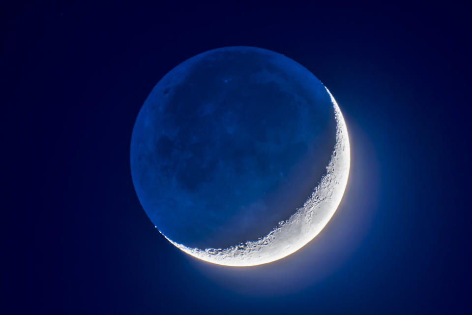 a thin crescent moon hangs in the night sky, while the 