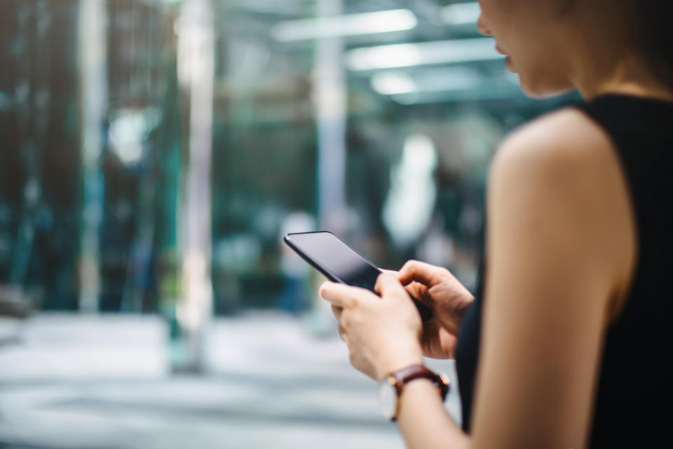 Close up of busy businesswoman emailing on mobile phone by office towers in downtown financial district