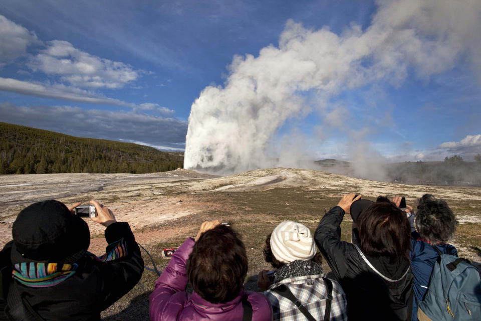 FILE - In this May 21, 2011 file photo, tourists photograph Old Faithful erupting on schedule late in the afternoon in Yellowstone National Park, Wyo. On Tuesday, March 24, 2020 the National Park Service announced that Yellowstone and Grand Teton National Parks would be closed until further notice, and no visitor access will be permitted to either park..(AP Photo/Julie Jacobson, File)