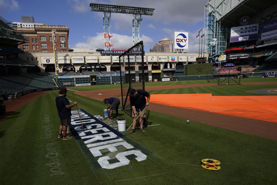 Stadium workers paint the logo on the field Monday, Oct. 25, 2021, in Houston, in preparation for Game 1 of baseball's World Series tomorrow between the Houston Astros and the Atlanta Braves. (AP Photo/David J. Phillip)