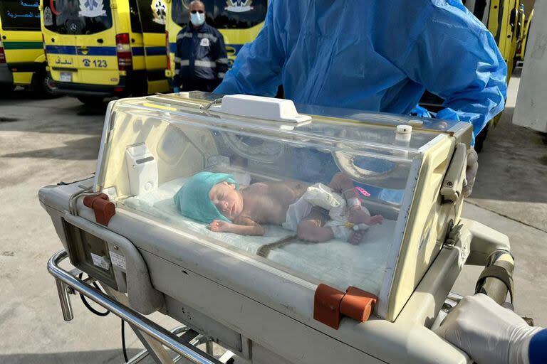 Médicos egipcios llevan en silla de ruedas a un bebé palestino prematuro evacuado de Gaza a una ambulancia en el lado egipcio del paso fronterizo de Rafah con la Franja de Gaza.