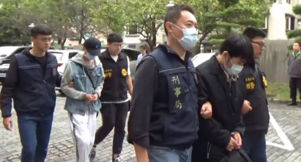 Two men are handcuffed and guided by two Taiwanese officers after an alleged $1.3 million insurance fraud bid.