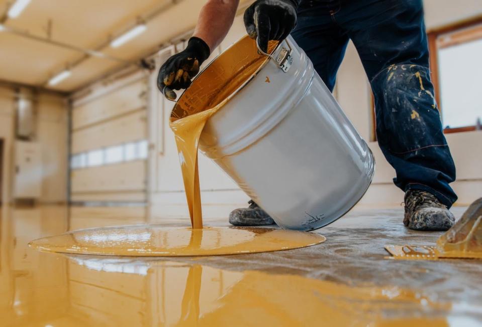 A close up of a worker pouring stain on a concrete floor.