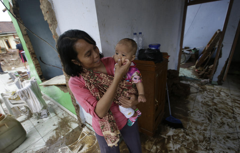 A woman holds her baby inside a destroyed house at a tsunami-area in Carita, Indonesia, Thursday, Dec. 27, 2018. Indonesia has widened the no-go zone around an island volcano that triggered a tsunami on the weekend, killing hundreds of people in Sumatra and Java. (AP Photo/Achmad Ibrahim)