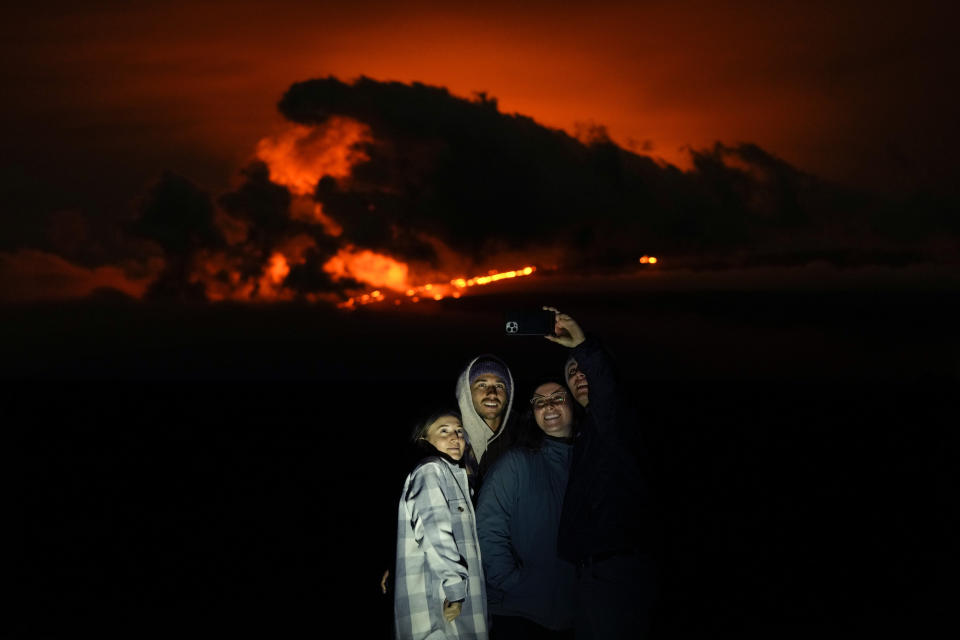 Ashlyn Nadeau, left, stands next to her husband, Casey Nadeau, second from left; Jessica Doyle, second from right, and Justin Potter, right, as they take a picture below the Mauna Loa volcano as it erupts Friday, Dec. 2, 2022, near Hilo, Hawaii. (AP Photo/Gregory Bull)