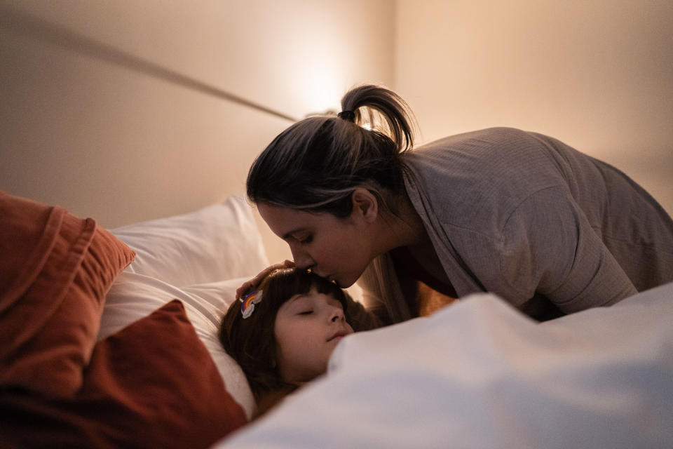 Woman kissing a child on the forehead and tucking them into bed