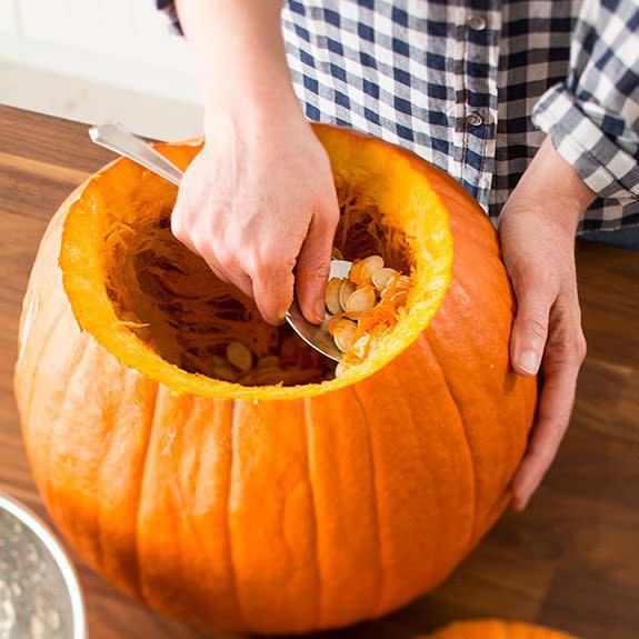 Person using a paddle to scoop out the seeds and gunk from the center of an open pumpkin