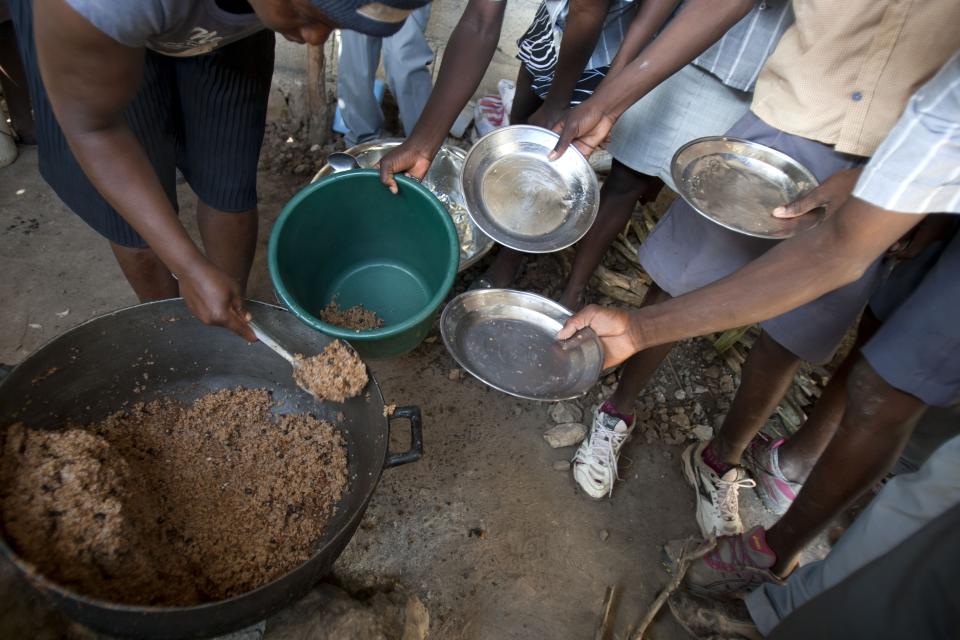 In this Tuesday, March 25, 2014 photo, students hold out their plates as the school cook ladles out a bulgur wheat and bean dish at a public school in Bombardopolis, Haiti. Drought is hitting one of the hungriest, most desolate parts of the most impoverished nation in the hemisphere and it has alarmed international aid organizations such the U.N.World Food Program, which sent workers this week to pass out bulgur wheat, cooking oil and salt. (AP Photo/Dieu Nalio Chery)