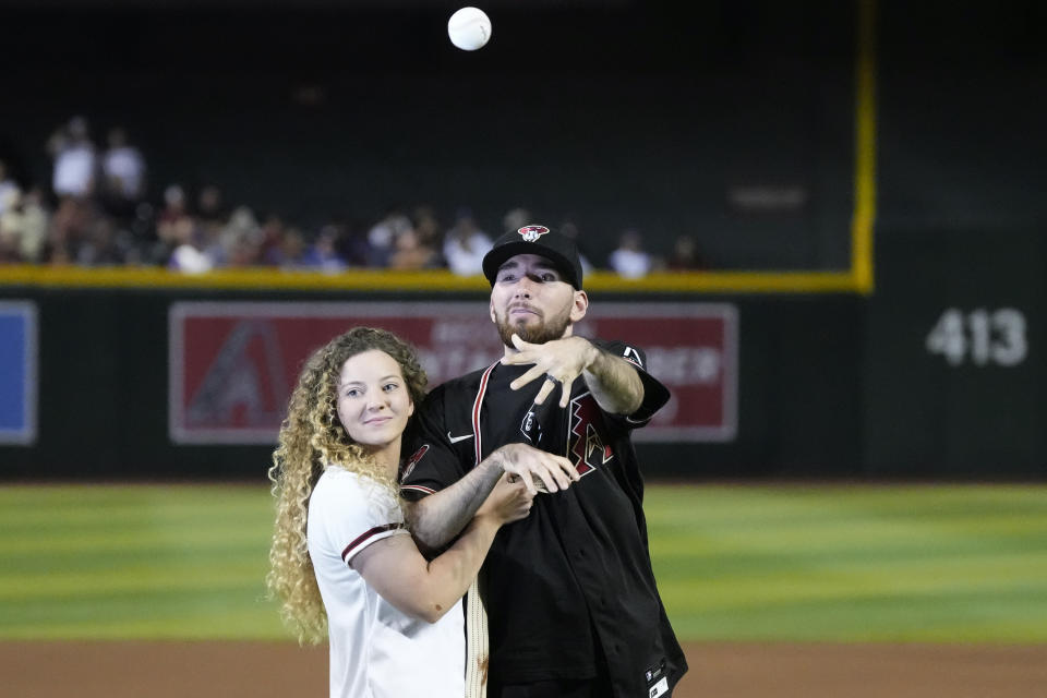 Phoenix Police Officer Tyler Moldovan, right, throws out the ceremonial first pitch as he is helped by wife Chelsea Moldovan prior to the Arizona Diamondbacks' home opening baseball game between against the Los Angeles Dodgers, Thursday, April 6, 2023, in Phoenix. Officer Molodvan was shot in the line of duty. (AP Photo/Ross D. Franklin)