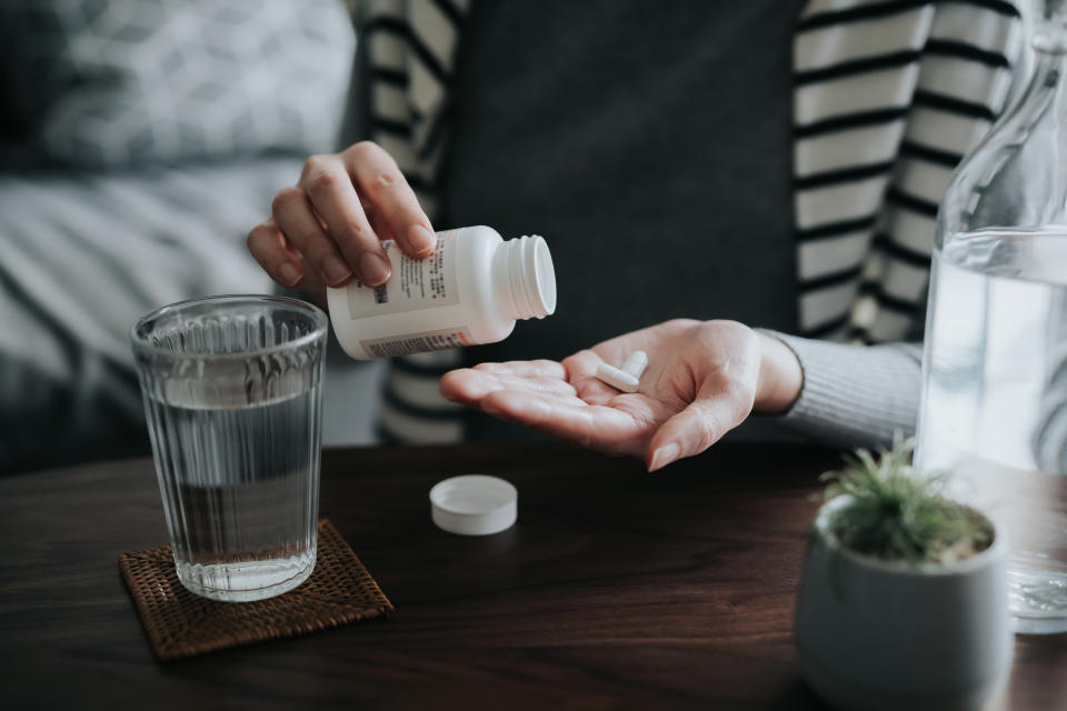 Close up of young Asian woman holding a pill bottle, pouring Tuberculosis pills into palm of hand, with a glass of water