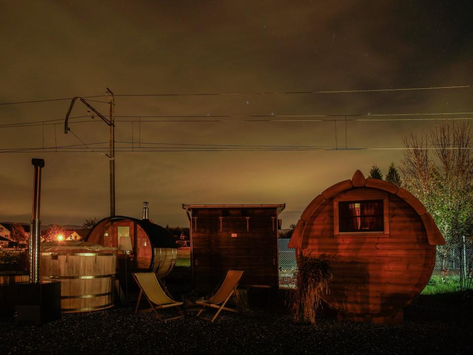 A cyclindrical tiny home next to another small building with two deck chairs in front of it, at night.