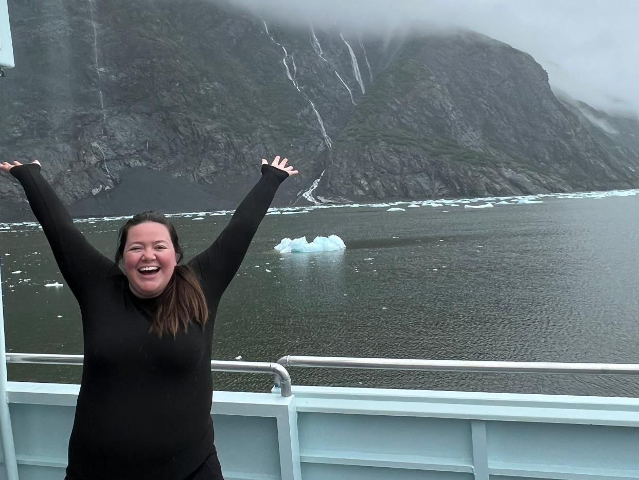 megan dubouis smiling with arms up in front of hazy glaciers on cruise