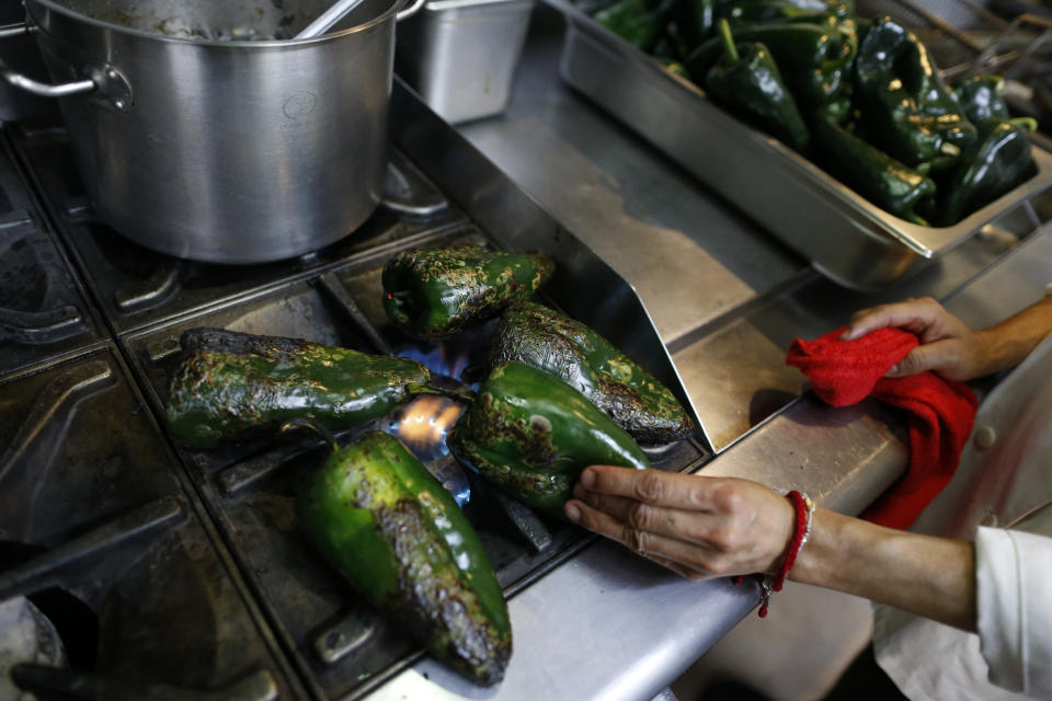 In this Sept. 13, 2019 photo, a cook roasts poblano peppers on the stovetop in preparation for removing the skin, as kitchen staff make chiles en nogada at Testal restaurant in downtown Mexico City. Testal has dedicated nearly an entire kitchen to the production of the emblematic dish, selling around 150 chiles per day, and attempting to more than double the 3000 chiles they sold last year during the short season. (AP Photo/Rebecca Blackwell)