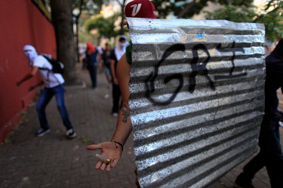 A demonstrator holding a metal sheet as a shield shows a rubber bullet casing fired by Bolivarian National Guards during clashes in Caracas, Venezuela, Sunday, March 2, 2014. Since mid-February, anti-government activists have been protesting high inflation, shortages of food stuffs and medicine, and violent crime in a nation with the world's largest proven oil reserves. (AP Photo/Rodrigo Abd)