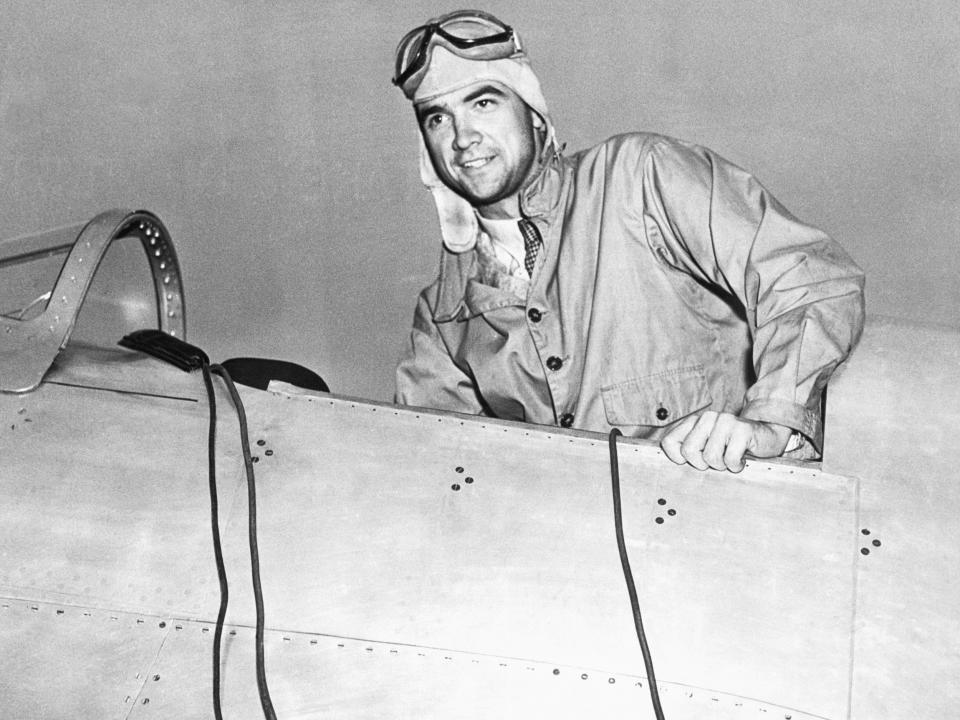 Howard Hughes in the cockpit of an airplane in a leather flight helmet and goggles.