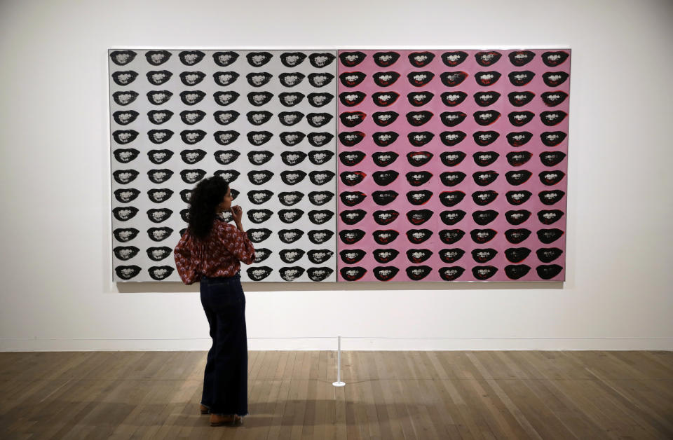 A Tate representative poses for photographs next to the 1962 Andy Warhol piece "Marilyn Monroe's Lips" during a media preview for the exhibition "Andy Warhol" at the Tate Modern gallery in London, Tuesday, March 10, 2020. The exhibition, which runs from March 12 to September 6, features over 100 works spanning the American artist's career in the second half of the 20th century until his death in 1987. (AP Photo/Matt Dunham)