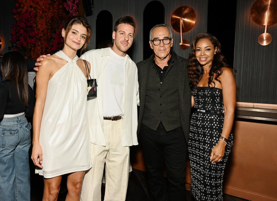 From left to right, a woman wearing a short white dress, Bradley Peltz wearing a white t shirt and button down with cream pants, an older man wearing a black top and pants, and a younger woman wearing a black printed dress