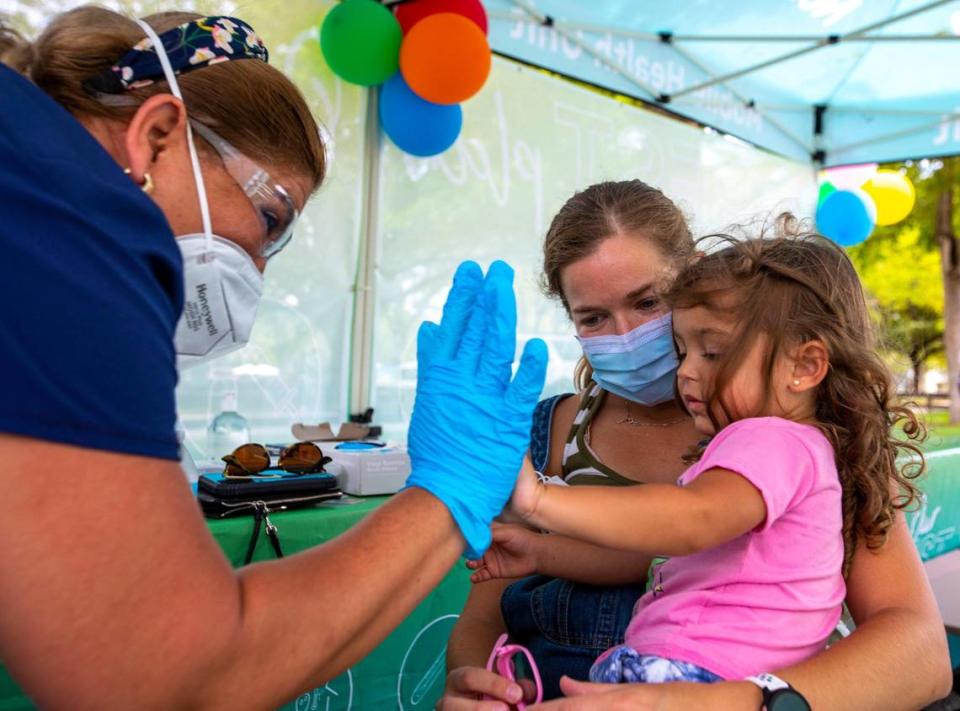 Westchester resident Julie Budejen, 35, holds her daughter Zoey, 3, as she high-fives a healthcare worker at the Nomi Health Mobile Health Unit inside Tropical Park in Miami, Florida, on Saturday, June 25, 2022. She has just received her COVID Pfizer vaccination as Saturday was the first day Miami-Dade County offered the free shots at eight sites. The vaccinations will continue on Sunday and throughout the week.