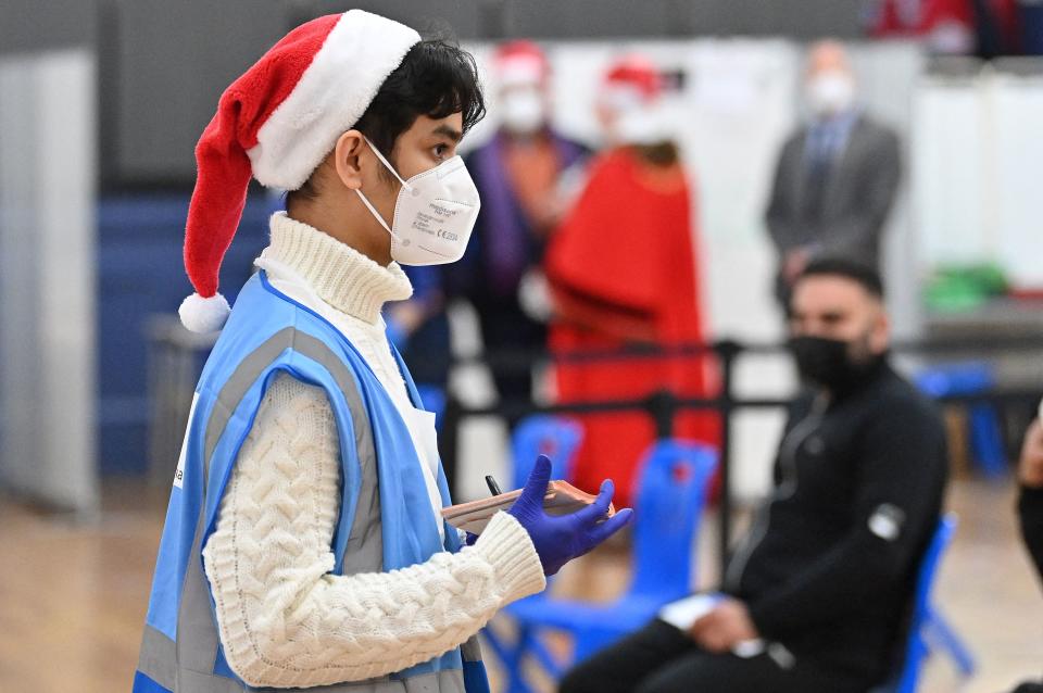 A health worker looks on as people wait to receive a dose of the Covid-19 vaccine at a pop-up coronavirus vaccination centre at the Redbridge Town Hall, east London on December 25, 2021. - British Prime Minister Boris Johnson in his Christmas Eve message exhorted the UK public to get jabbed as a 