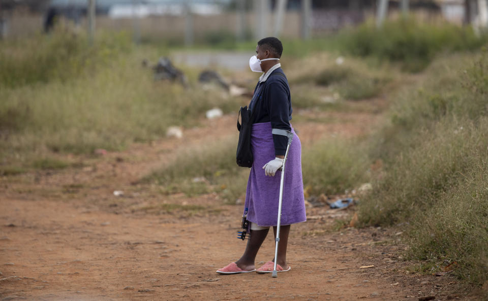 Noxolo Mbatha, wearing face masks and surgical gloves to protect herself against coronavirus, awaits a taxi for her hospital appointment at a informal settlement, east of Johannesburg, South Africa, Friday, March 27, 2020. The new coronavirus causes mild or moderate symptoms for most people, but for some, especially older adults and people with existing health problems, it can cause more severe illness or death. (AP Photo/Themba Hadebe)
