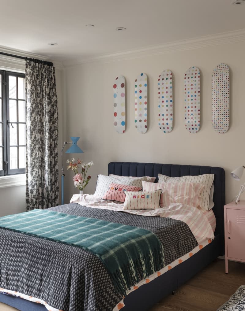 Bedroom with decorative art made of skateboards and colorful pillows next to a large window.