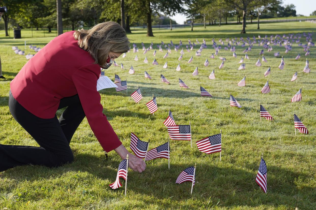 House Speaker Nancy Pelosi kneels to look at small flags placed on the grounds of the National Mall by activists from the COVID Memorial Project to mark the deaths of 200,000 lives lost in the U.S. to COVID-19 on Tuesday, Sept. 22, 2020 in Washington, D.C.