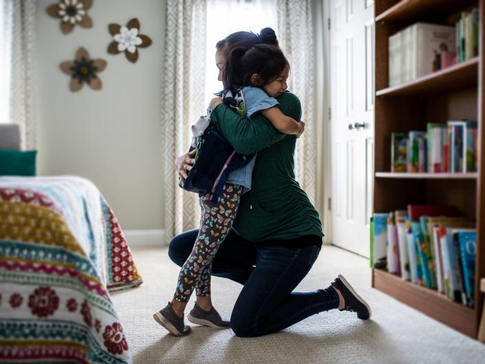 Mother embracing young daughter before school