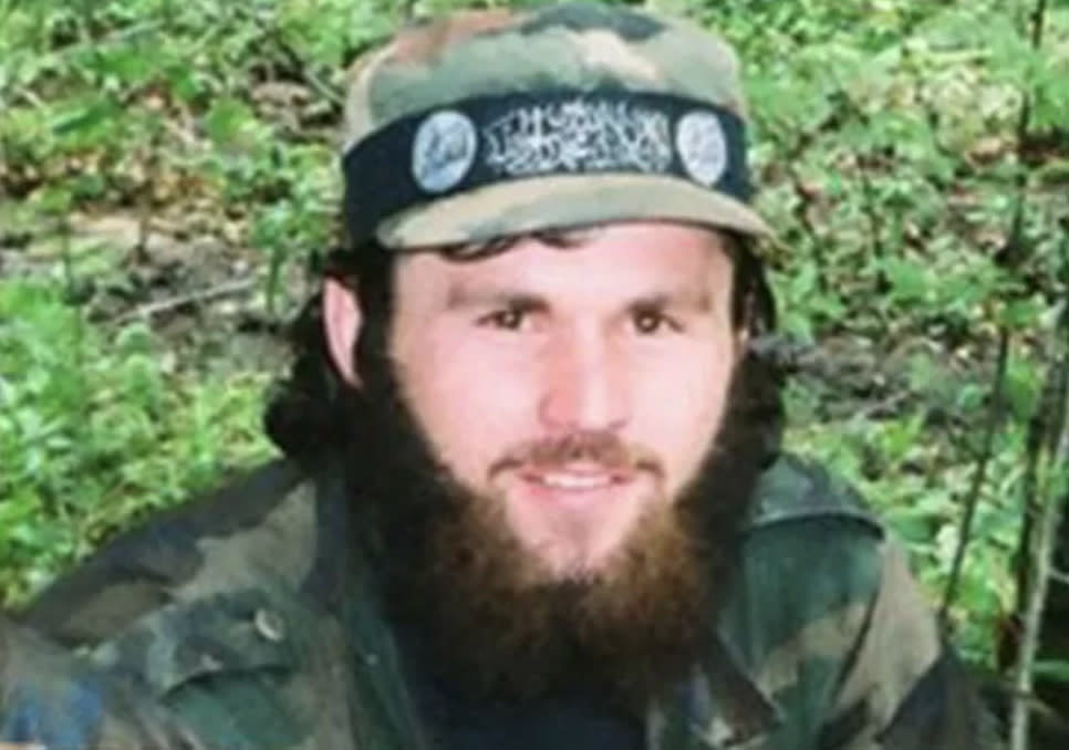 An undated photo shows a cheerful-looking Zelimkhan Khangoshvili in battle fatigues against a backdrop of vegetation, wearing a military cap with a band in Arabic script.
