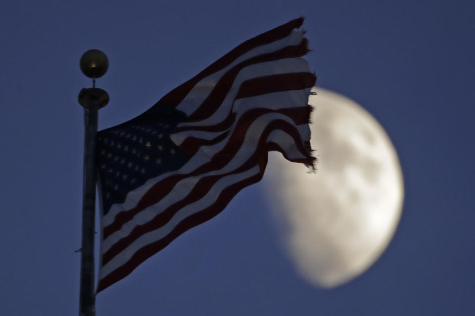 A flag flies in the wind above City Hall as the waxing gibbous moon passes behind clouds overhead Monday, June 29, 2020, in Kansas City, Mo. (AP Photo/Charlie Riedel)