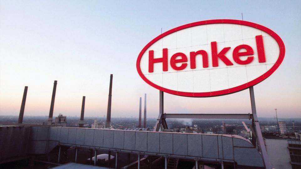 Henkel Logo über der Fabrik in Düsseldorf. Im Hintergrund sieht man hohe Schornsteine.