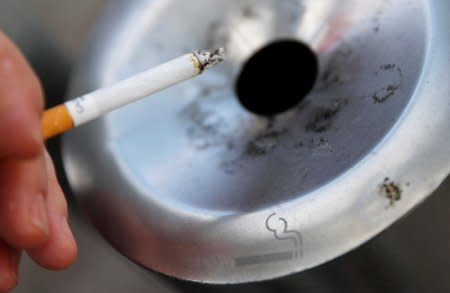 FILE PHOTO: A smoker holds his cigarette while standing next to an ashtray at a smoker's corner near the soccer stadium in Wolfsburg, Germany, April 6, 2016.    REUTERS/Kai Pfaffenbach