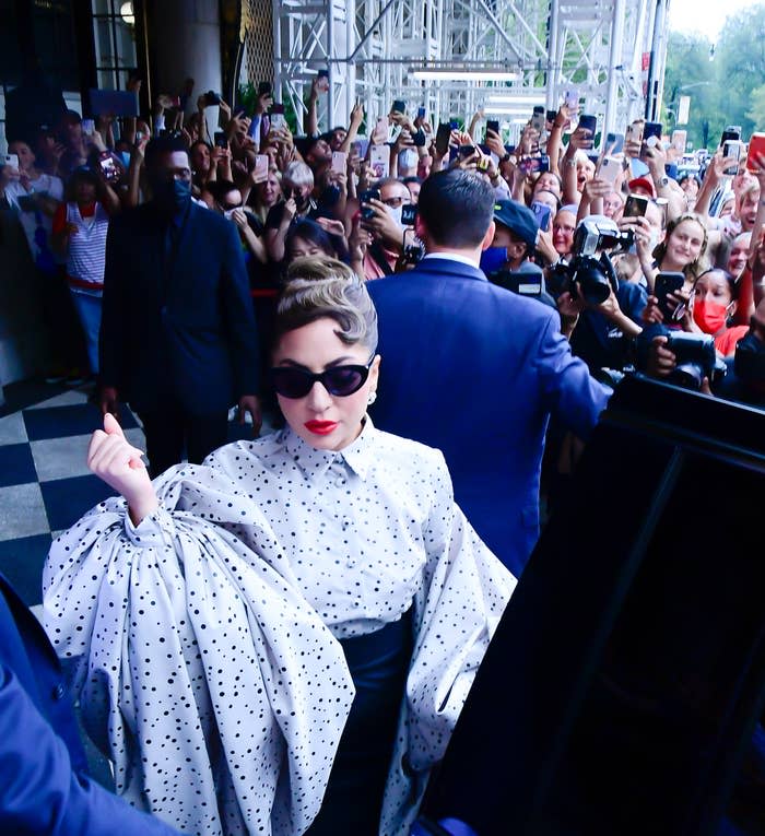 Lady Gaga wears a polka dot blouse with voluminous sleeves and sunglasses as she walks past a crowd of fans