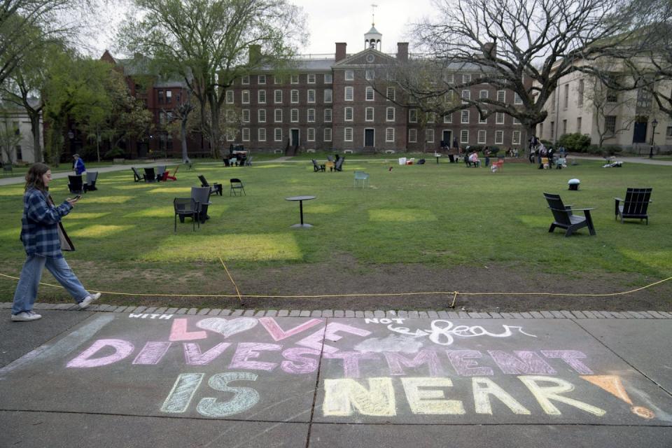 A message in chalk decorates a sidewalk on a college campus, including the words 'Divestment is near.'