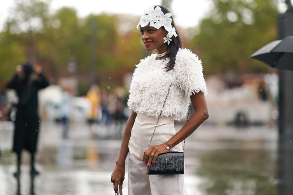 PARIS, FRANCE - OCTOBER 01: A guest wears a white lace headband, earrings, pearl necklaces, a white fluffy short sleeves top, white pants, a shiny black bag, outside Chanel, during Paris Fashion Week - Womenswear Spring Summer 2020, on October 01, 2019 in Paris, France. (Photo by Edward Berthelot/Getty Images)