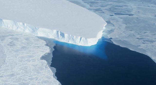 A giant white glacier floats on top of blue water.