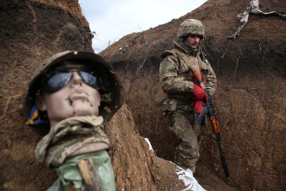 An Ukrainian serviceman walks in a trench by a sort of mannequin as he stands at his post on the frontline with Russia backed separatists near the town of Zolote, in the Lugansk region on April 8, 2021.