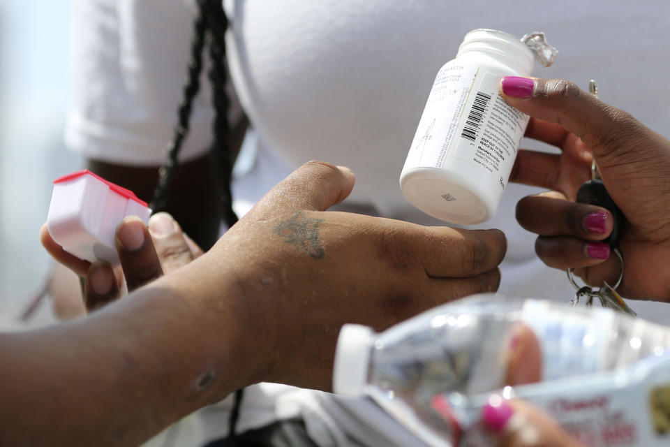 In this Wednesday, July 24, 2019, photo Ivette Naida, left, receives her HIV medication from social workers from the IDEA Exchange. Naida is part of the University of Miami sponsored IDEA Exchange program, which provides HIV-infected homeless drug users with secure pill lockers for their medicine, or can deliver the medicine to them. Naida, who was diagnosed with HIV more than a decade ago, lives underneath a Miami highway overpass and has no safe place to keep her belongings. (AP Photo/Lynne Sladky)