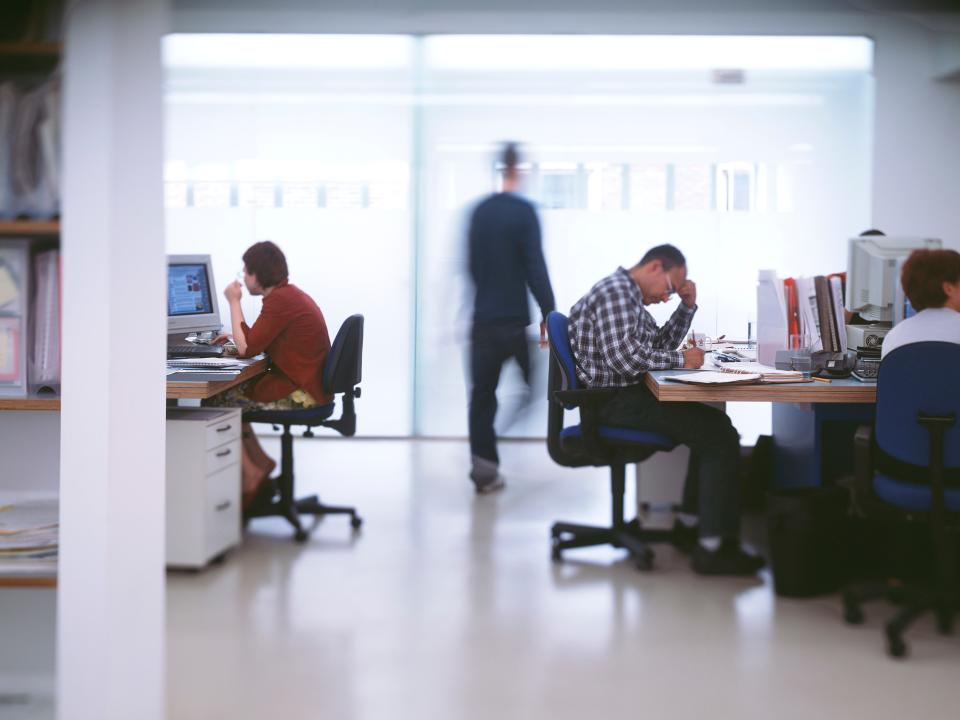 A modern-style office with people sitting at desks and working on computers in front of a large glass window.