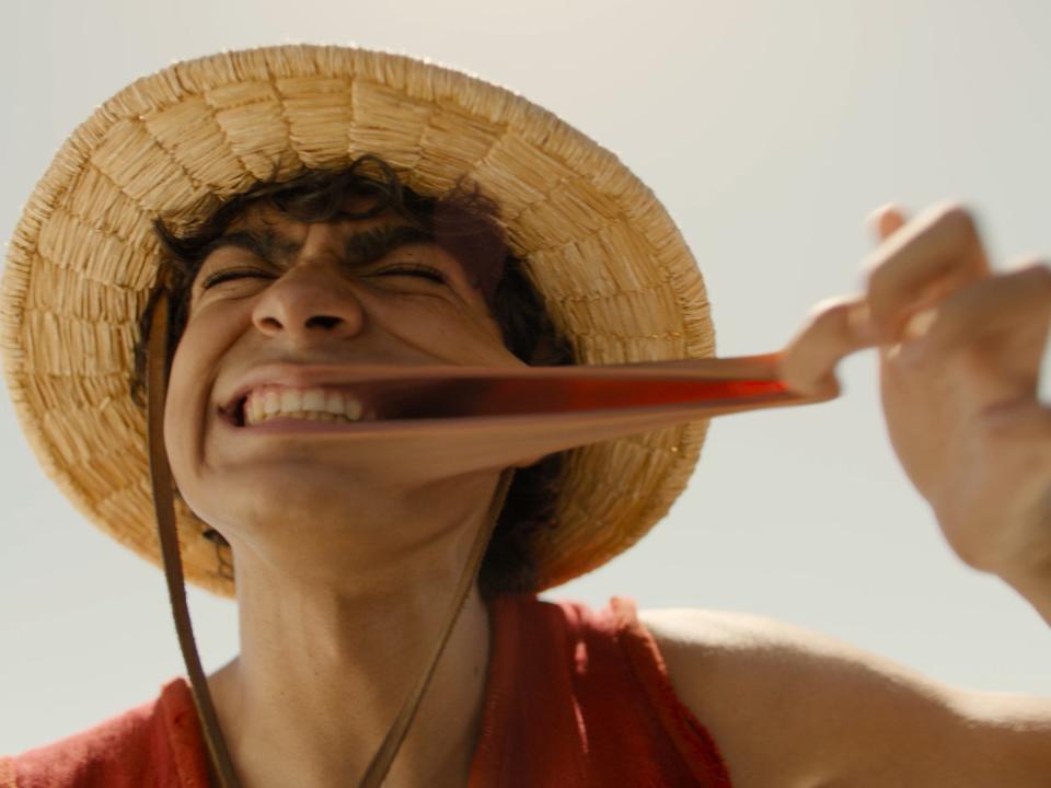 iñaki godoy as luffy in netflix's one piece. he's stretching out his cheek, demonstrating that he can stretch like rubber, and grinning widely