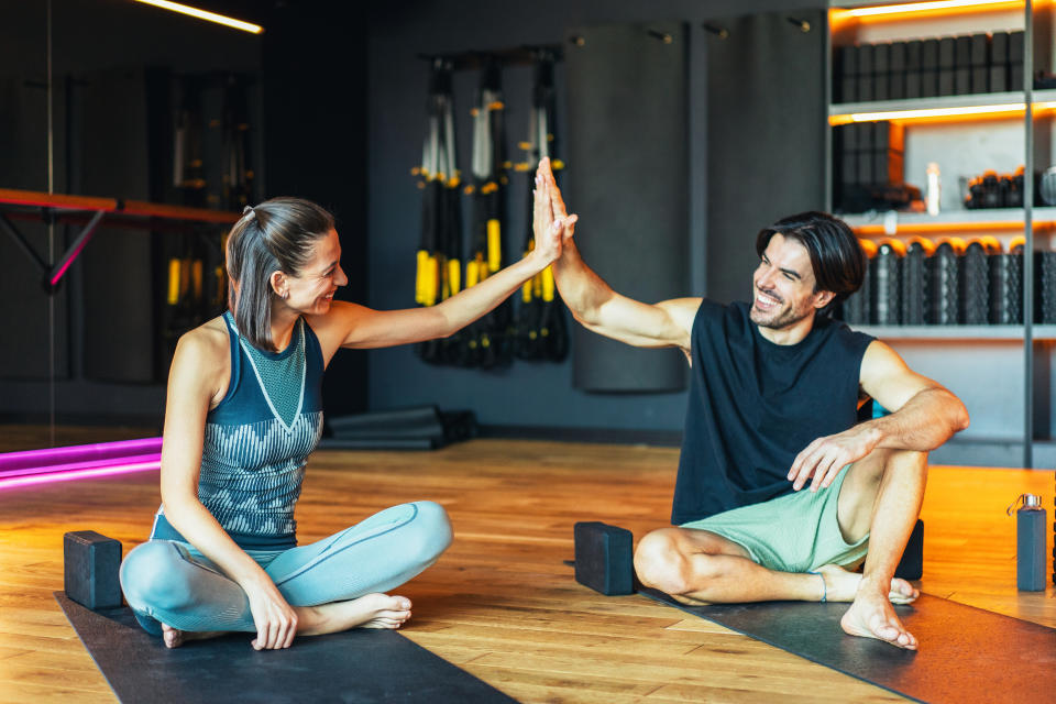 Woman and man sitting on yoga mats in a gym and giving each other a high five