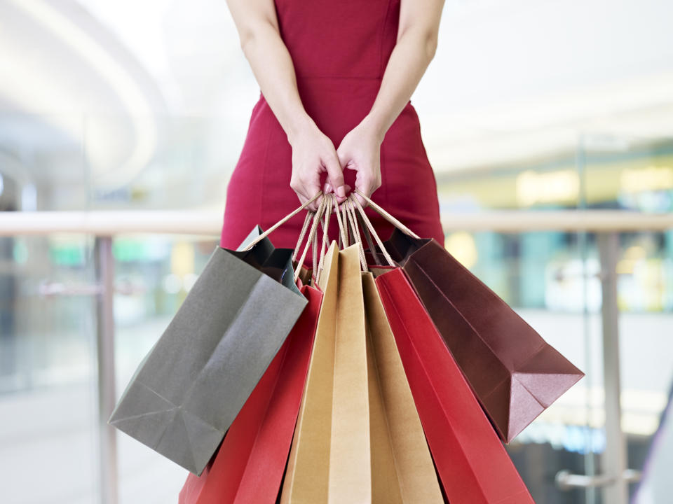 young woman female shopper standing with colorful paper bags in hands in shopping mall or department store, focus on hands
