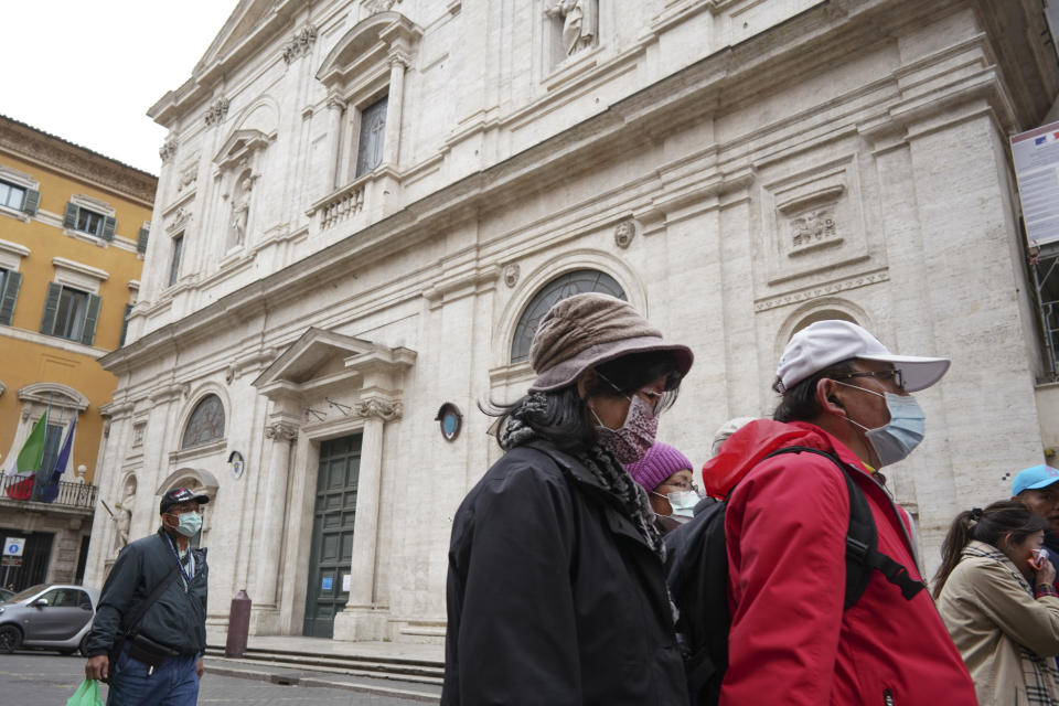 Tourists wearing protective masks walk past the St. Louis of the French church in Rome, Sunday, March 1, 2020. The French community church in Rome, St. Louis of the French, closed its doors to the public on Sunday, reportedly after a priest was infected with a new virus. The church in the historic center of Rome is famous for three paintings by the Baroque master Caravaggio, and is a tourist draw. A sign on the door Sunday noted in French that the church had been closed as a precaution by the French Embassy for both Masses and touristic visits until further notice. (AP Photo/Andrew Medichini)