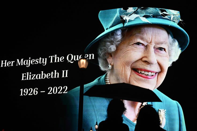 TOPSHOT - Members of the public stop in the rain to study a huge picture of Britain's Queen Elizabeth II displayed at Piccadilly Circus in central London on September 8, 2022, after the announcement of the death of Queen Elizabeth II, in central London. - Queen Elizabeth II, the longest-serving monarch in British history and an icon instantly recognisable to billions of people around the world, has died aged 96, Buckingham Palace said on Thursday. (Photo by Ben Stansall / AFP) (Photo by BEN STANSALL/AFP via Getty Images)