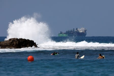 FILE PHOTO: People surf as a vessel involved in the construction of a natural gas pipeline is seen behind them in the Mediterranean Sea near Dor Beach